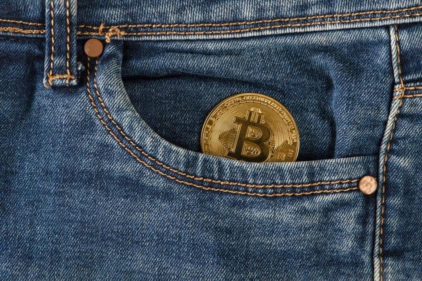 Una moneda de bitcoin dorada yace en el bolsillo de unos jeans.