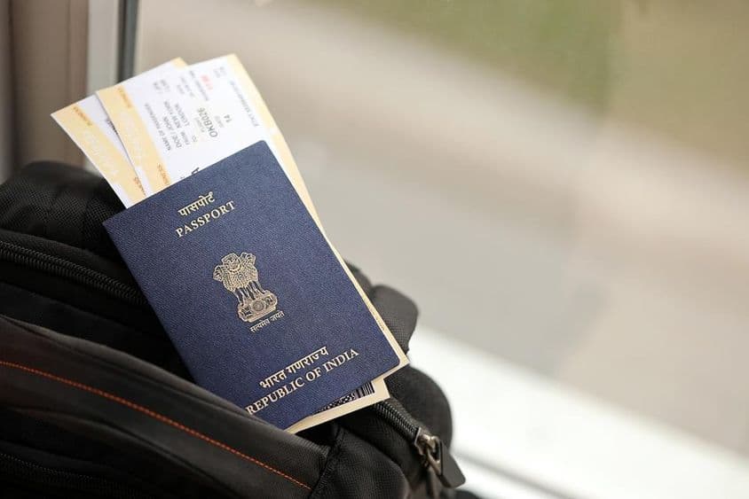 Pasaporte indio azul con boletos de avión sobre una mochila de viaje.