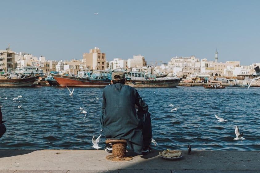Hombre disfrutando de la vista frente al mar con barcos y gaviotas en Dubai Creek.