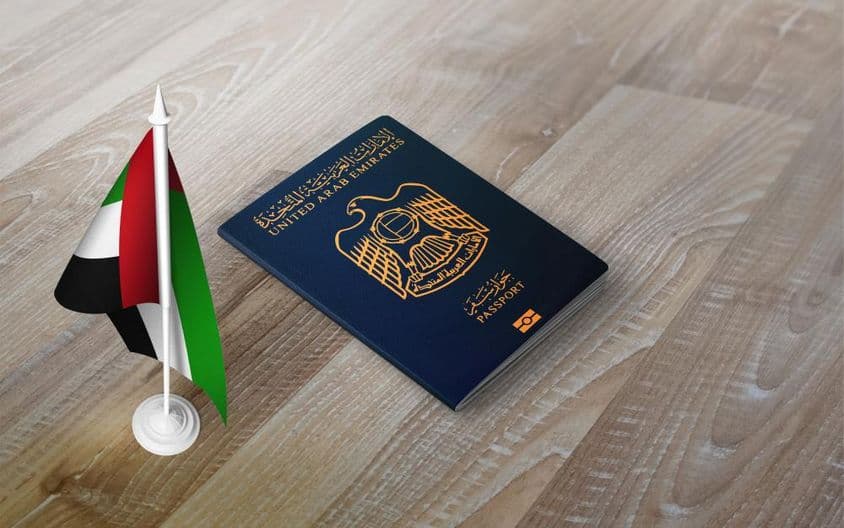 Pasaporte de los Emiratos Árabes Unidos sobre una superficie de madera, con una bandera nacional.