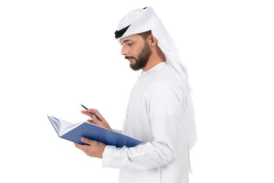 Joven maestro árabe de pie escribiendo en el libro.