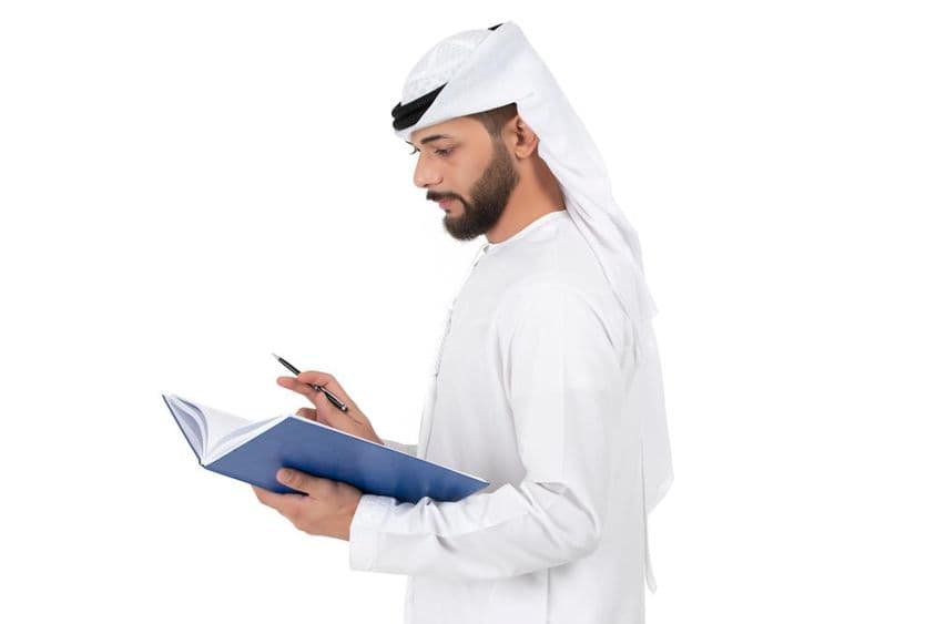 Joven maestro árabe de pie escribiendo en el libro.