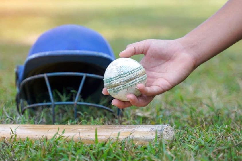 La mano de un jugador recogiendo una pelota de cricket entre otros equipos de cricket en el césped.