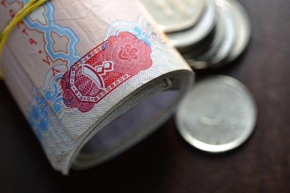 Dirhams de los EAU enrollados acompañados de unas pocas monedas.