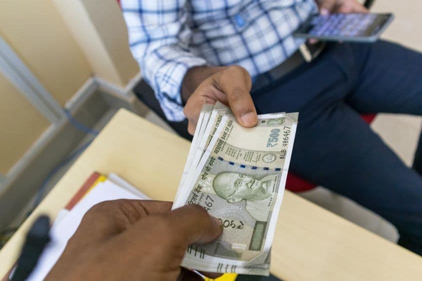 Una persona entregando un billete indio de 500 rupias a otra persona.