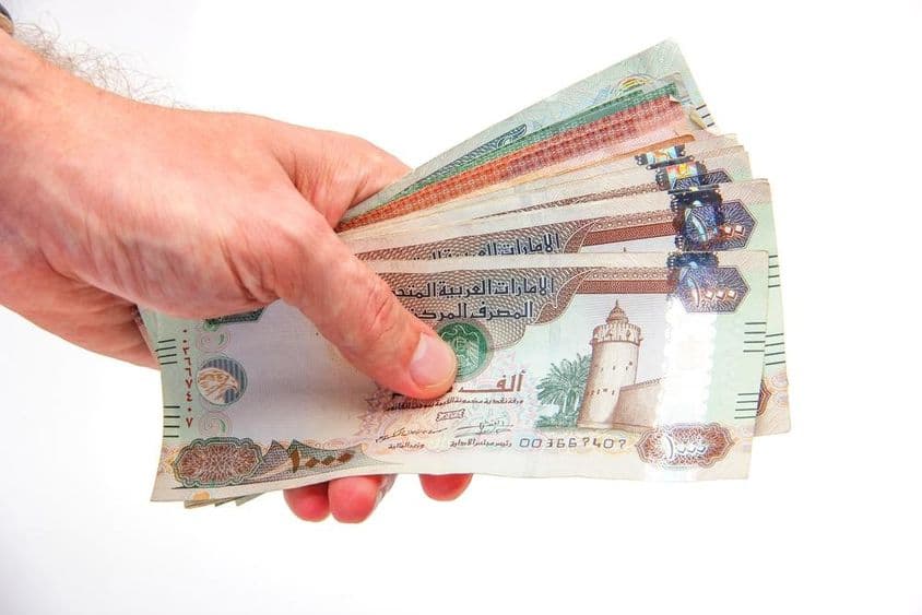 Un hombre sosteniendo billetes de dirhams de los Emiratos Árabes Unidos.