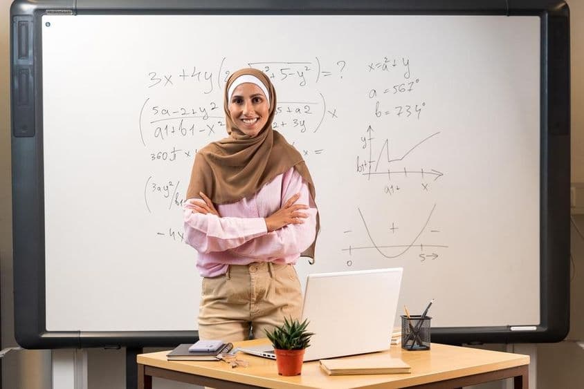 Mujer árabe docente en hijab parada en el aula.