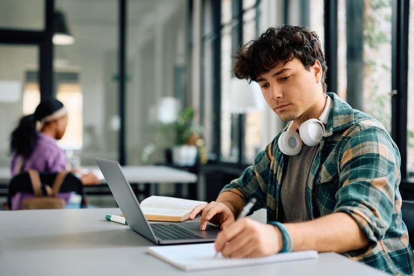 Estudiante universitario usando una laptop mientras escribe.