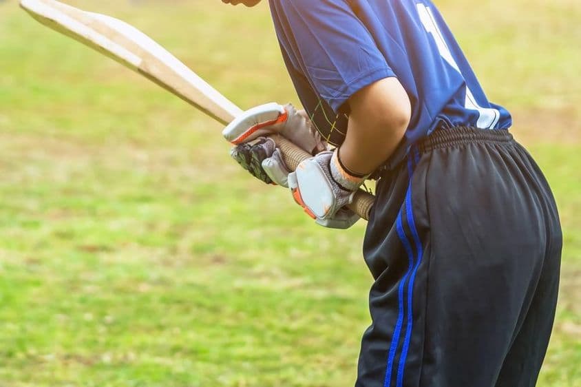 Joven jugadora asiática de críquet con equipo protector bateando una pelota en el campo.