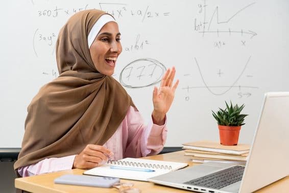 Maestra en hijab saludando a estudiantes durante una clase en línea.