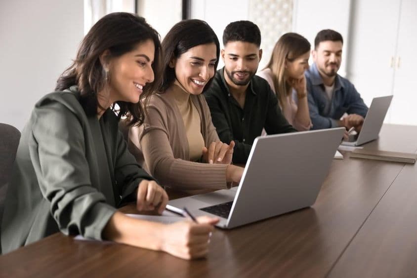 Estudiantes jóvenes adultos multinacionales estudiando con laptops en un centro educativo.