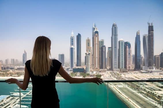 Una mujer de negro con mirada pensativa en un balcón con vista a los rascacielos de Dubái, Emiratos Árabes Unidos.