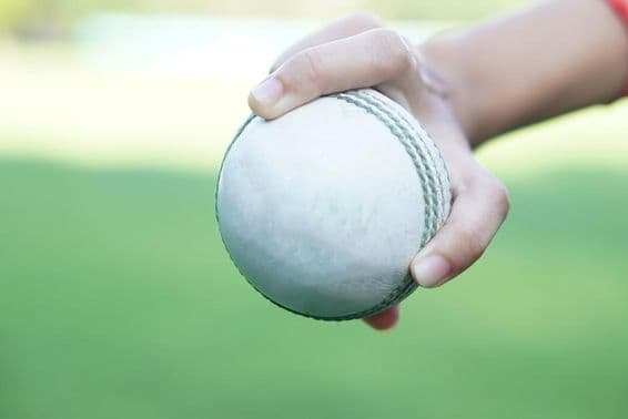 Un jugador de críquet sosteniendo una bola de críquet de cuero blanco.