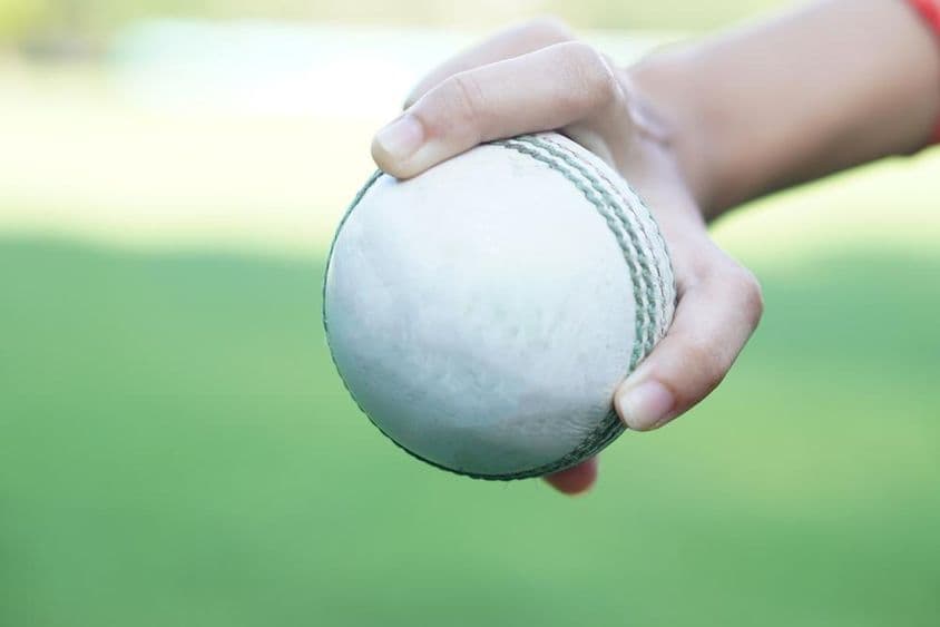 Un jugador de críquet sosteniendo una bola de críquet de cuero blanco.