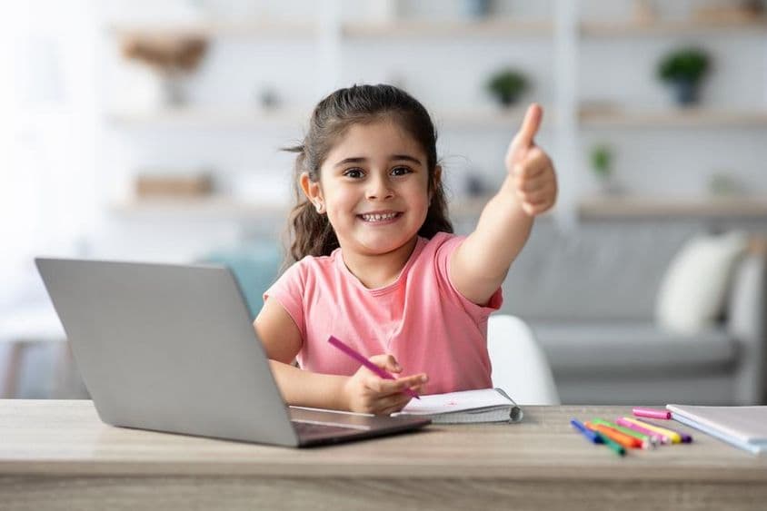 Niña árabe aprendiendo en casa con un portátil, mostrando el pulgar arriba.