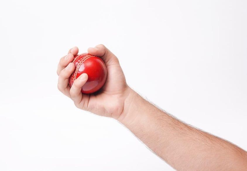 Un jugador de cricket masculino agarrando firmemente una pelota de cricket roja.