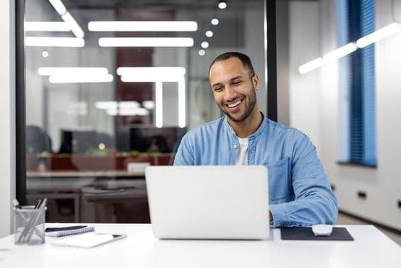Un joven profesional feliz sonriendo mientras trabaja en una computadora.