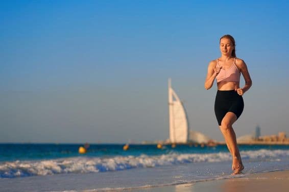 Mujer joven corriendo en verano en Dubái con Burj Al Arab de fondo.
