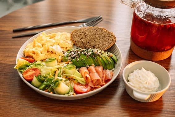 Desayuno saludable con huevos, aguacate, verduras, ensalada y té de frambuesa.