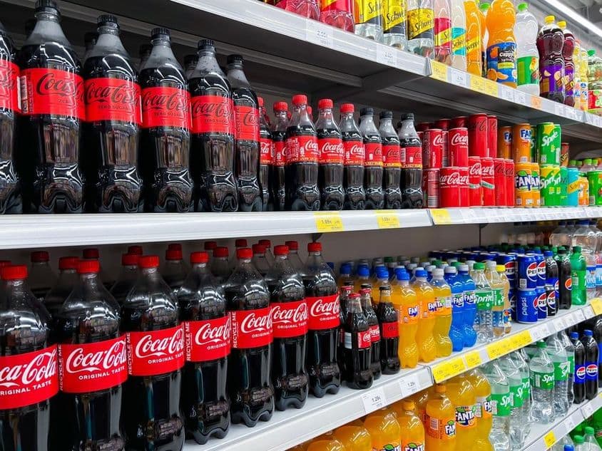 Fila de botellas de cola en una estantería de supermercado.