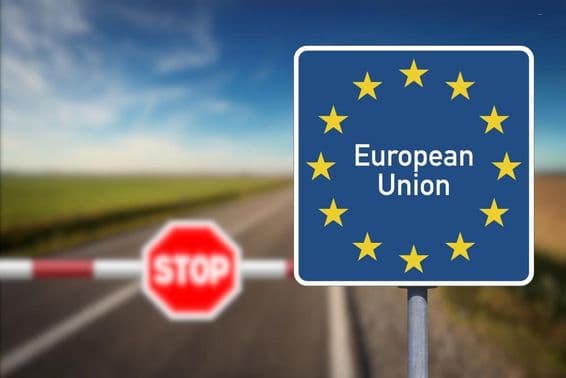 Emblema de la Unión Europea y un cruce fronterizo con barrera y señal de stop.