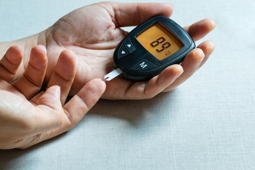 Manos de un hombre usando un medidor digital de glucosa en sangre para monitorear la diabetes.