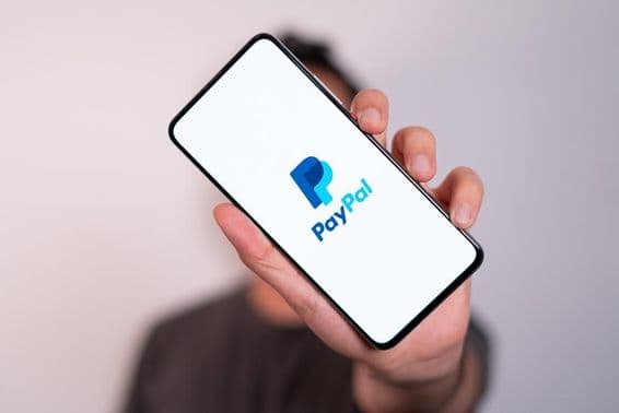 Un hombre sosteniendo un teléfono con el logotipo de PayPal visible en la pantalla del teléfono.