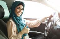 Mujer árabe feliz en hijab conduciendo su auto con pulgar arriba.