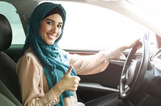 Mujer árabe feliz en hijab conduciendo su auto con pulgar arriba.