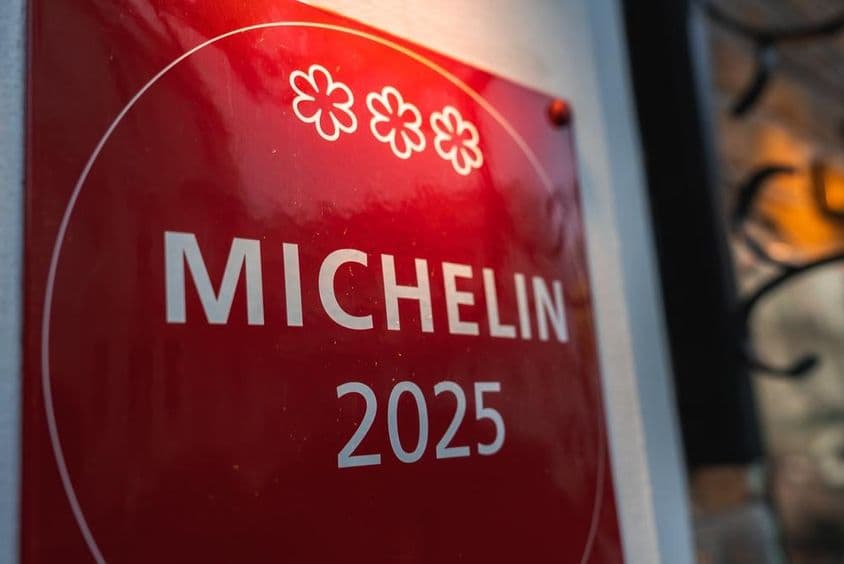 Una placa Michelin 2025 de tres estrellas roja en una pared de color claro.