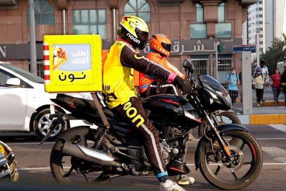 Repartidor en motocicleta entregando en una calle de Dubai.