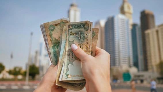 Una niña sosteniendo moneda de EAU con rascacielos de Dubai al fondo.