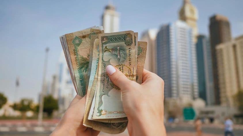 Una niña sosteniendo moneda de EAU con rascacielos de Dubai al fondo.