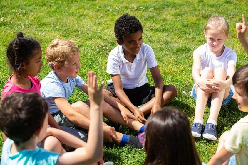 Niños de primaria conversando en el césped verde.
