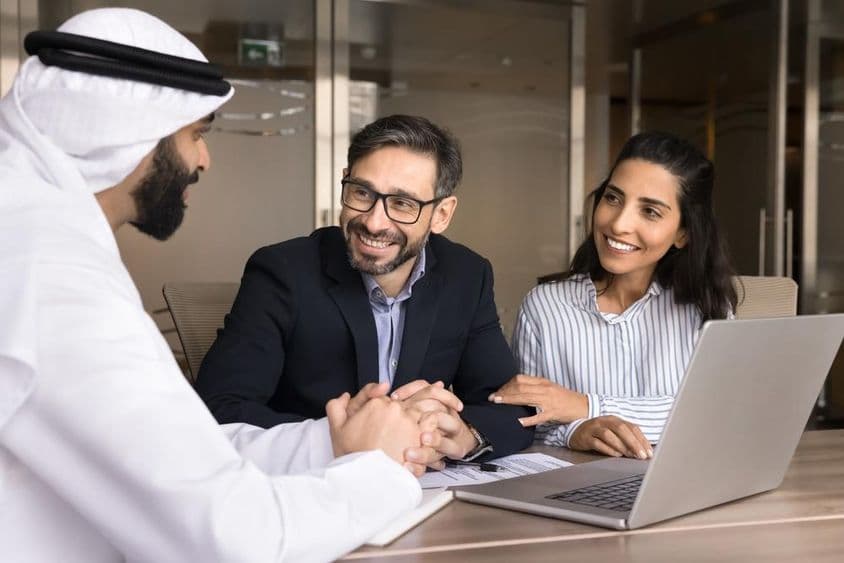 Una pareja latina feliz reuniéndose con un agente inmobiliario árabe.