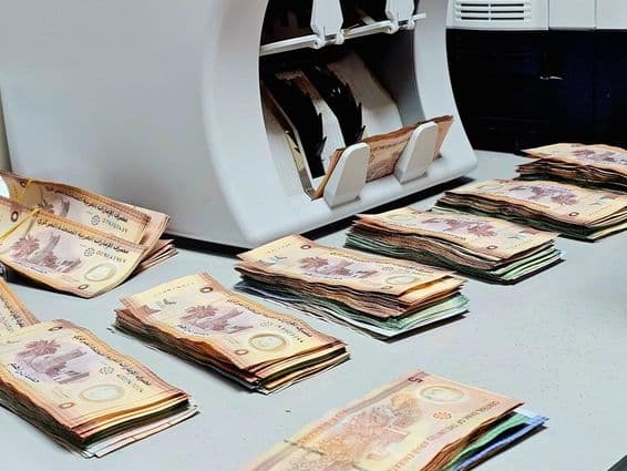 Máquina contadora de billetes con fajos ordenados de billetes de dirham emiratí en una mesa.