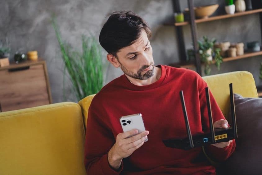 Un joven relajándose en casa con un smartphone y router, disfrutando de una tarde tranquila.