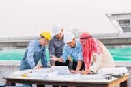 Empresario árabe, ingeniero y obrero interactúan con planos de construcción usando una laptop.