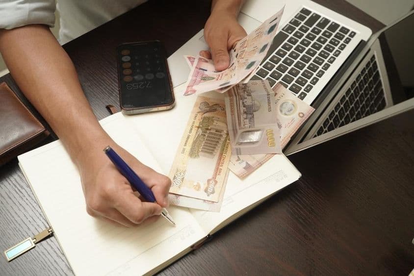 Un hombre sentado en un escritorio contando un montón de billetes de dirham de EAU.