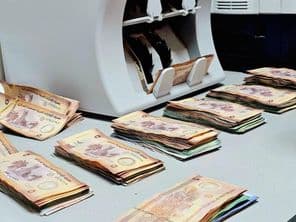Máquina contadora de dinero con fajos ordenados de billetes de dirham emiratí en un escritorio.