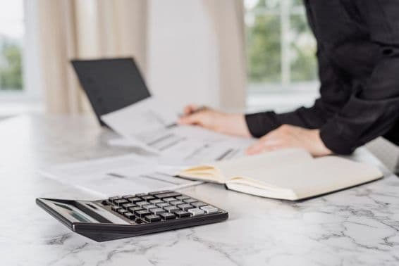 Una mujer vestida de negro calculando gastos con una laptop.