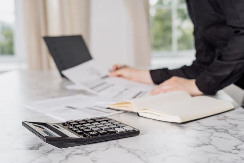 Una mujer vestida de negro calculando gastos con una laptop.