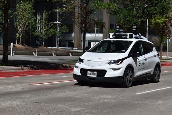 Un coche autónomo supervisado blanco circulando en el distrito financiero del centro.
