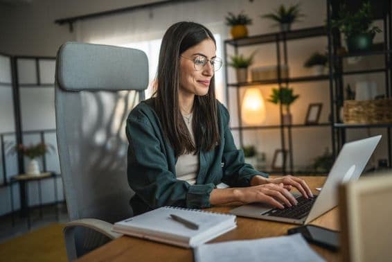 Mujer adulta trabajando en una laptop y usando un cuaderno en una oficina en casa.