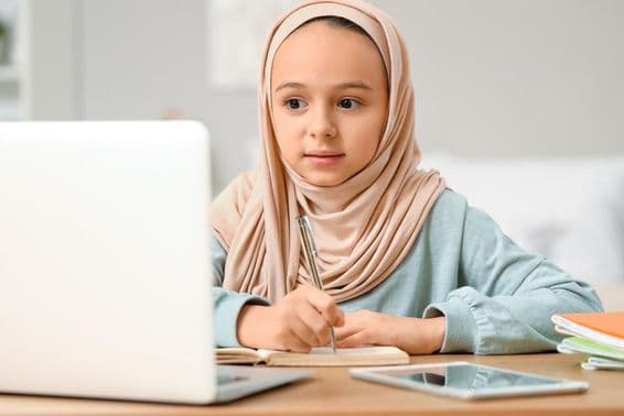 Niña musulmana pequeña con hijab haciendo tarea en casa.