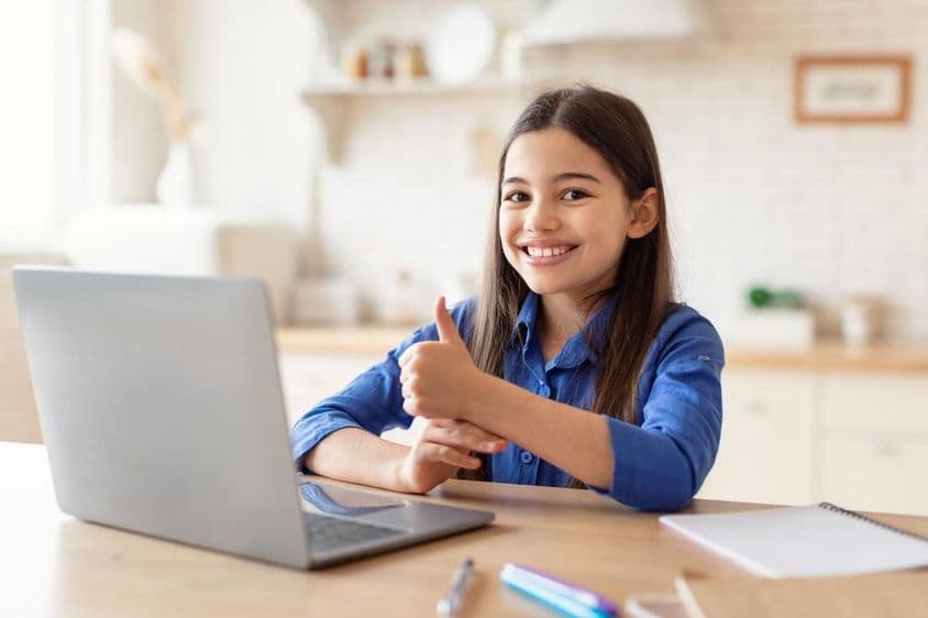 Niña del Medio Oriente feliz estudiando en línea con una computadora portátil.