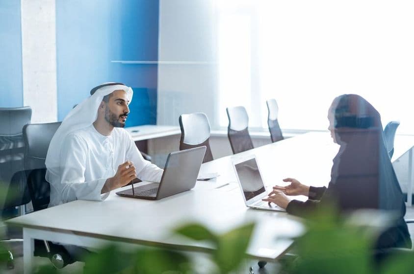 Hombre y mujer con vestimenta tradicional trabajando en una oficina comercial en Dubái.