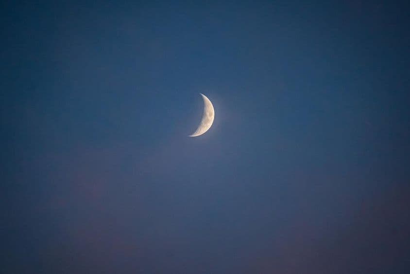 Luna creciente al anochecer con nubes susurrantes.