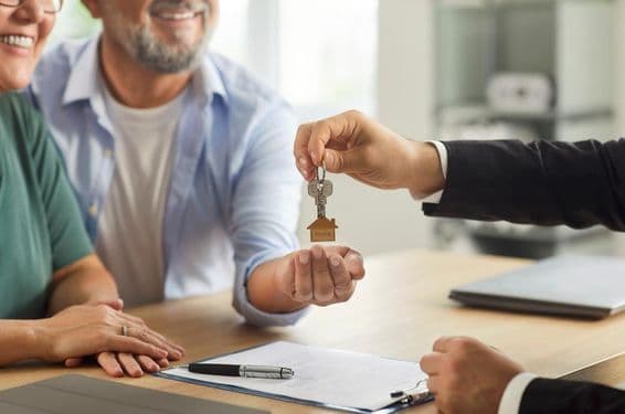 Un agente inmobiliario entregando llaves a una pareja de ancianos sonriente.