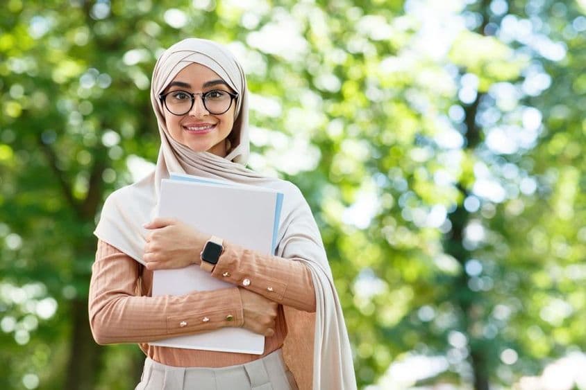 De vuelta a la escuela, mujer árabe con hijab y gafas sosteniendo libros en el parque.
